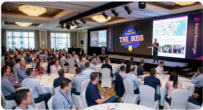 Conference audience watching the finale for Who Kidnapped Your Boss on a large stage screen.