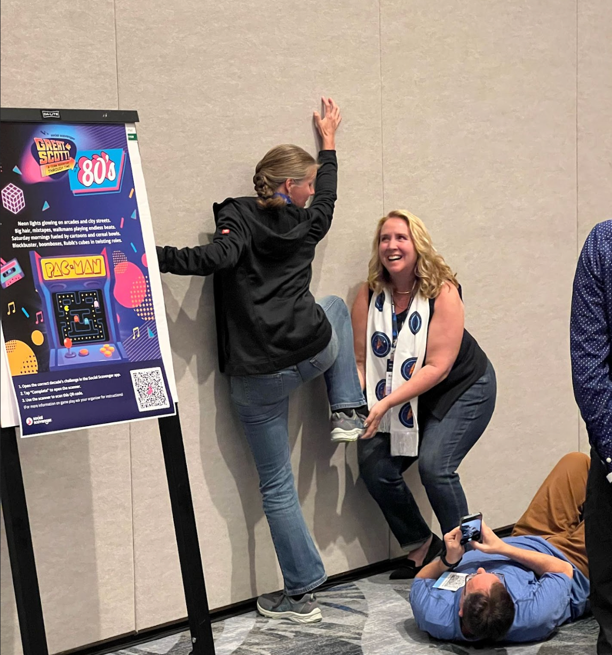 Two players engaging with the 80s decade poster at a Great Scott! event.